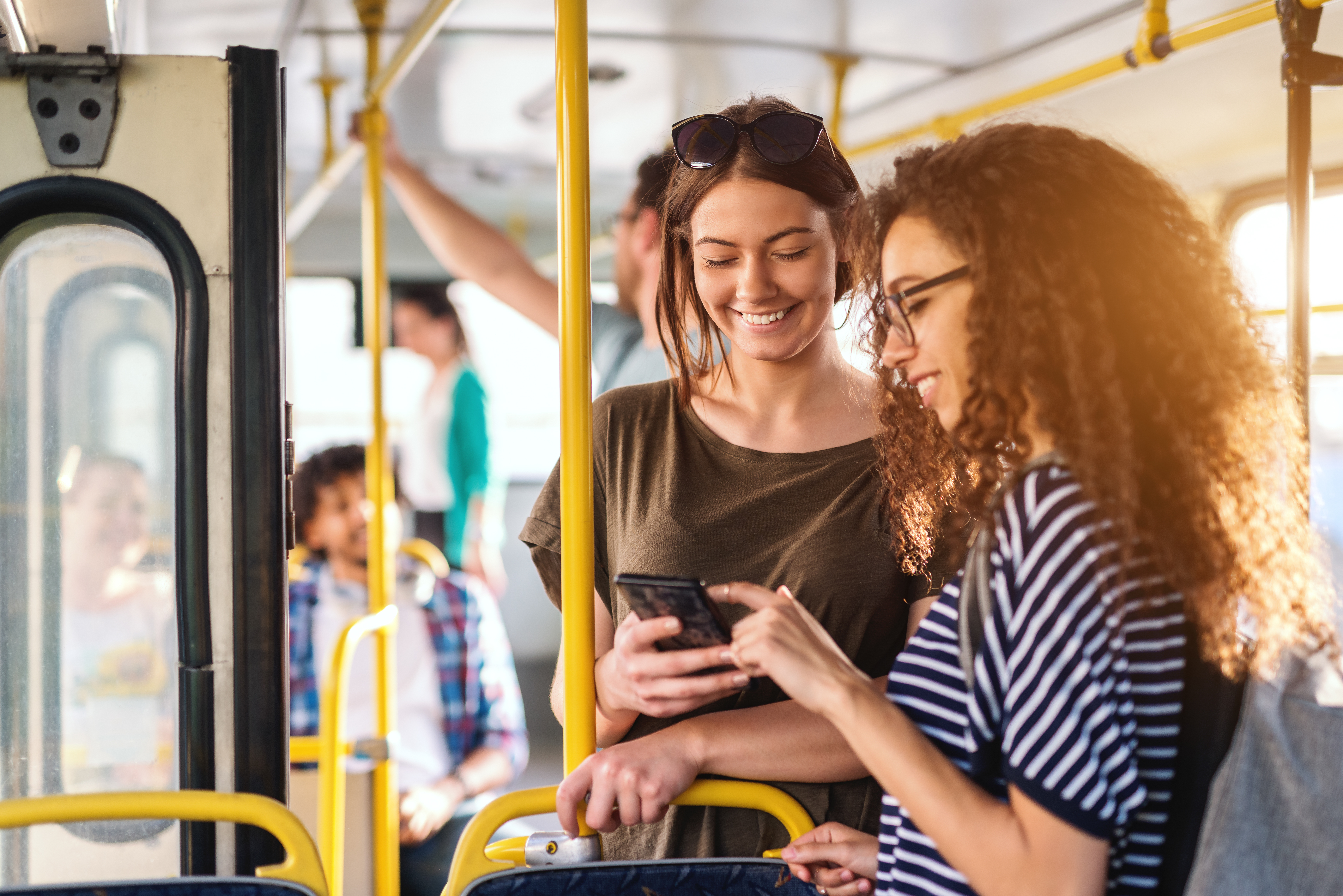 Young women smile as they look at mobile phone on bus